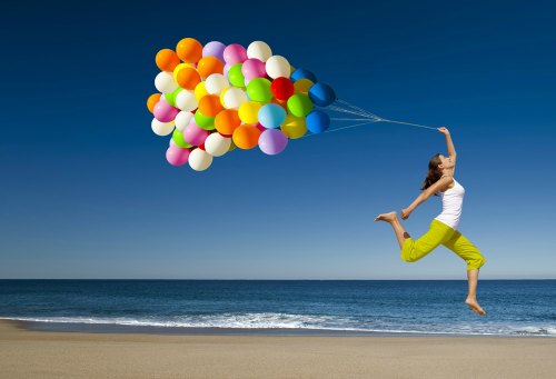 Beautiful and athletic girl with colorful balloons jumping on the beach
